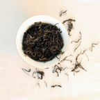 Dry whole leaves of Himalayan Golden Black tea with shimmering golden tips in a white bowl