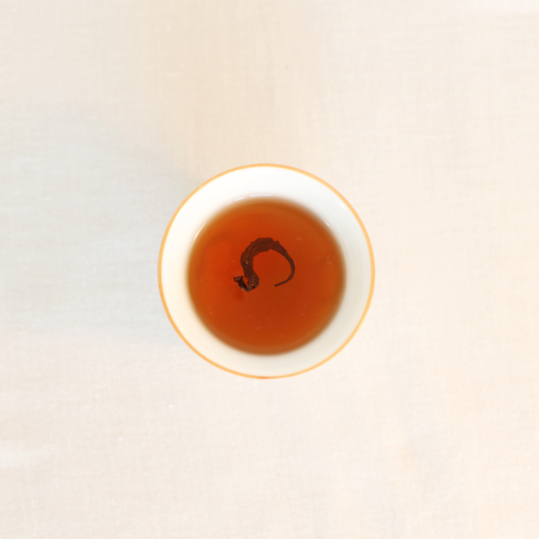 Brewed Rare Red Oolong Himalayan tea, rich amber liquor in a white ceramic cup