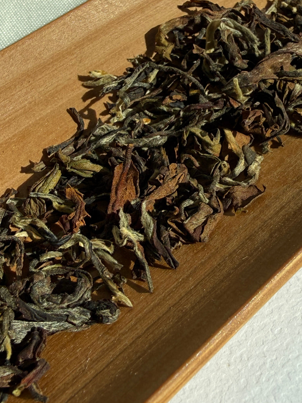 Dry Pekoe Hill leaves on a wooden board in sunlight, showing the silver tips, olive green and copper brown typical of a bug-bitten oolong
