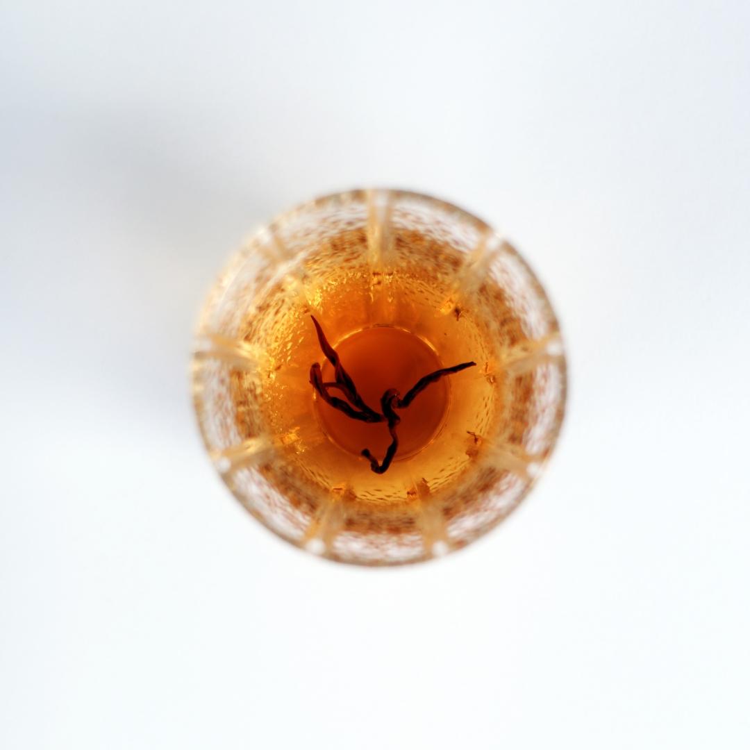 Close-up of brewed Himalayan Golden Black tea, golden amber liquor in a glass tea cup.