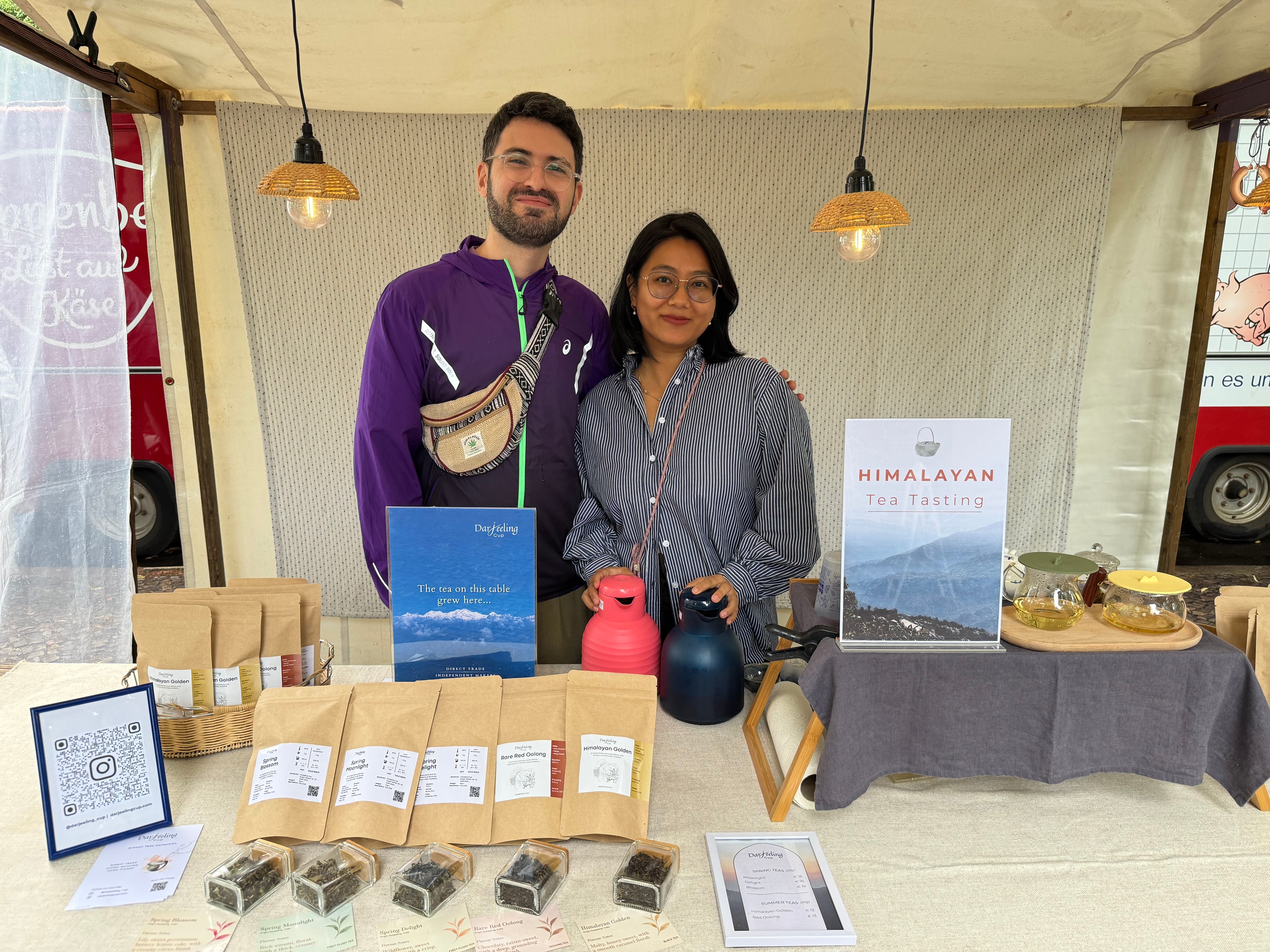 Alen and Swikriti behind the Himali Cup market stall in Berlin, with pouches of loose-leaf tea and a Himalayan tea tasting sign
