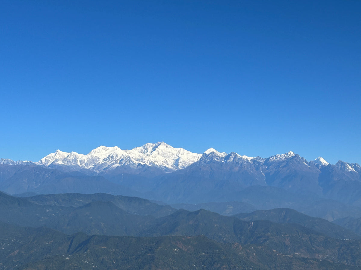 The snow-capped Kangchenjunga range rising above forested ridges in the Himalayan hills under a clear blue sky