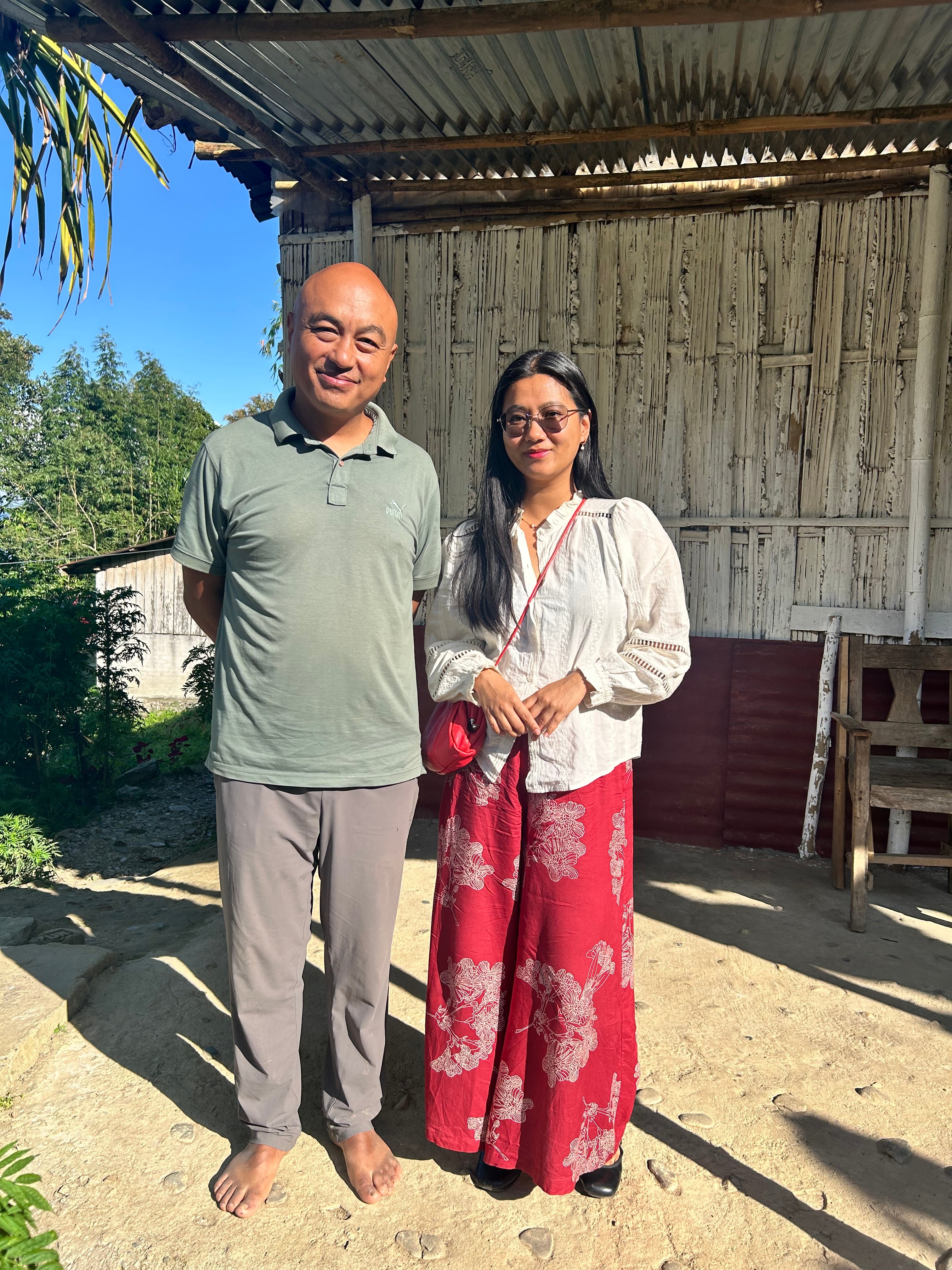Sonam and Swikriti standing together outside a bamboo-walled house in the Darjeeling hills