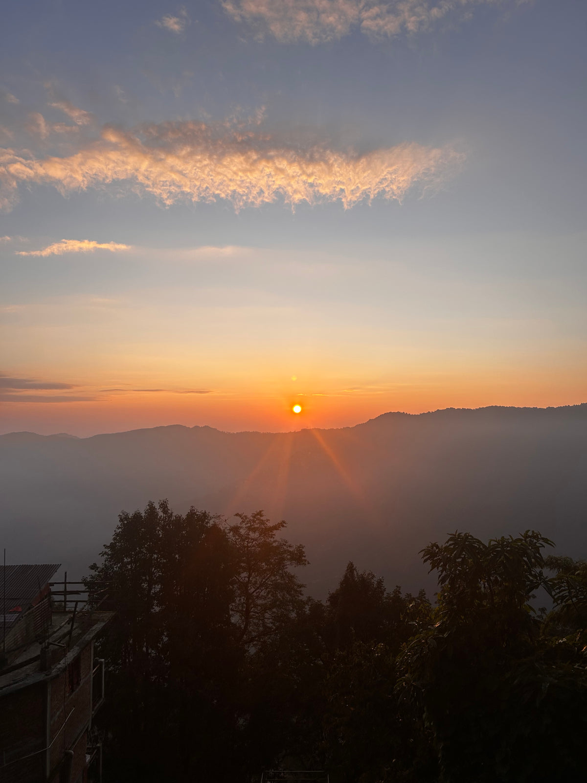 Sunrise over layered ridges in the Darjeeling hills, the sun low on the horizon and mist filling the valleys