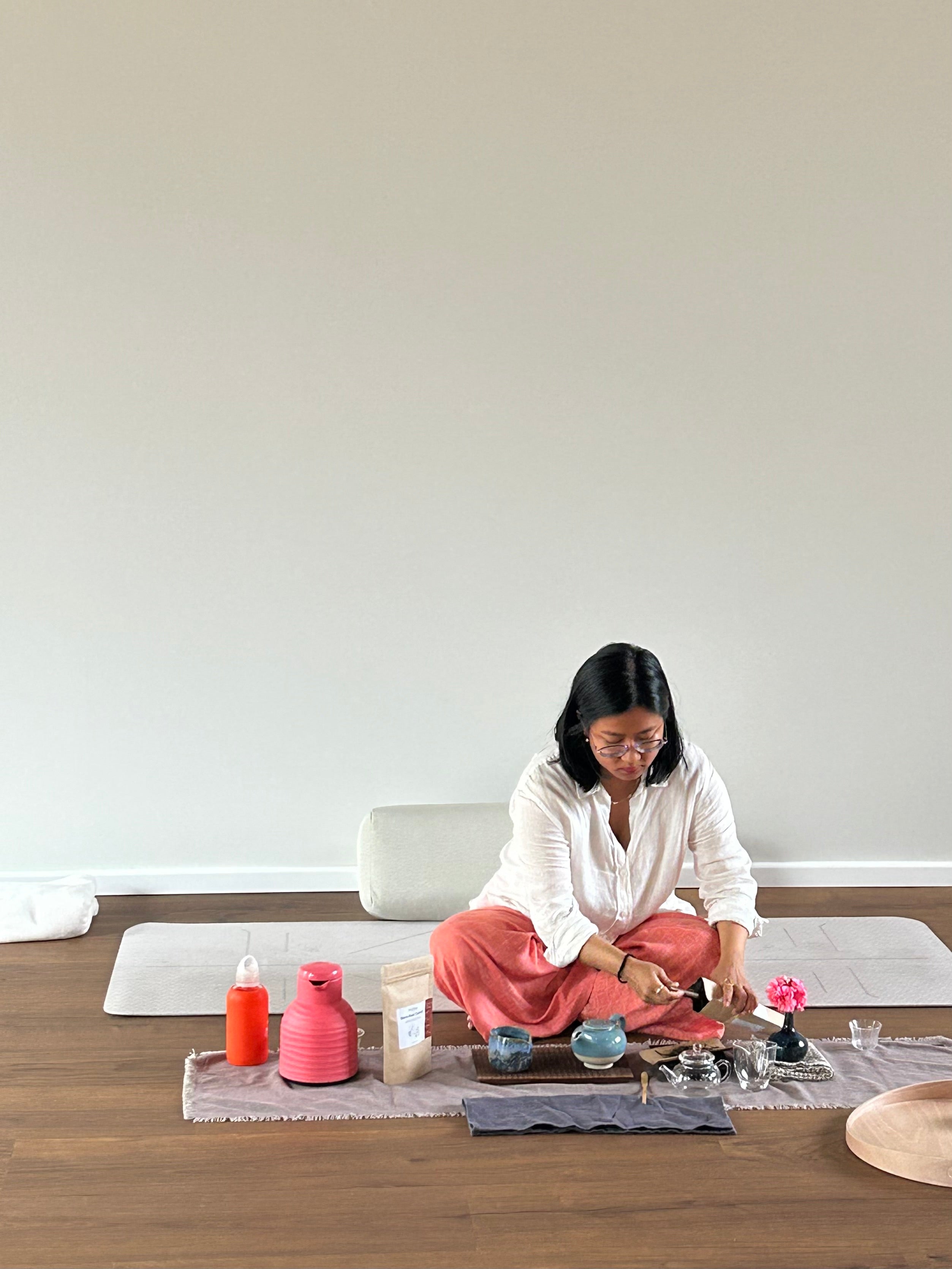 Swikriti sitting cross-legged on a mat, laying out a tea tasting with small cups, a pot and a pouch of loose leaf