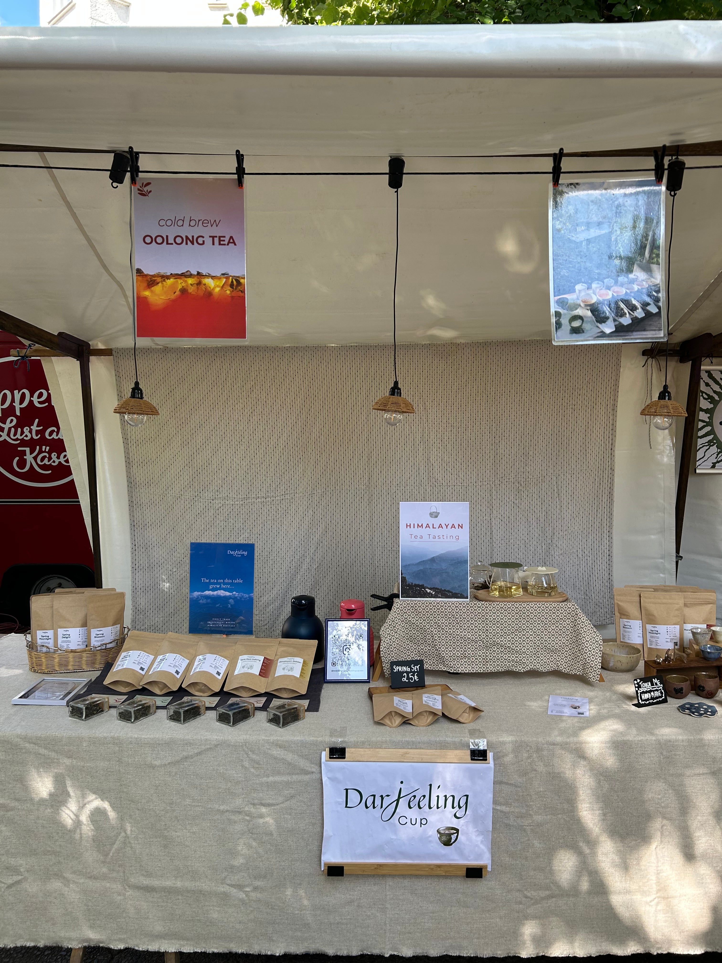 The Himali Cup market stall in Berlin under a white canopy, with pouches of loose-leaf tea, a cold brew oolong poster and a tasting table