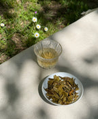 Spring Delight T78 & AV2 First Flush brewed in a glass cup with whole dark green leaves on a linen surface outdoors