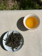 Spring Blossom AV2 First Flush dry leaves and warm golden liquor in a ceramic cup viewed from above on linen