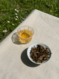 Spring Blossom AV2 First Flush brewed in a glass cup with brewed whole leaves on a linen surface in natural sunlight
