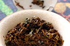 Infused Himalayan Beauty leaves in a white crackle-glaze bowl after brewing. This oolong is bug-bitten, which gives it candied orange peel and honey notes.