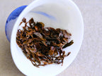 Aufgegossene Blätter von Pine Forest, einem gerösteten Schwarztee mit Noten von getrockneten Pflaumen, entfaltet in einem schräg gestellten weiß-blauen Gaiwan