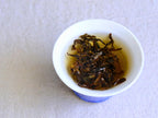 Pine Forest Schwarztee zieht in einem weißen Gaiwan mit blauem Fuß, die entfalteten Blätter in einem goldenen Aufguss