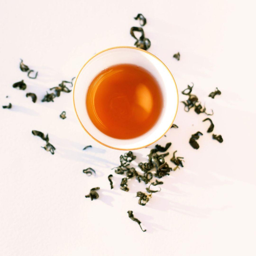 Rare Red Oolong, brewed cup surrounded by loose dry leaves