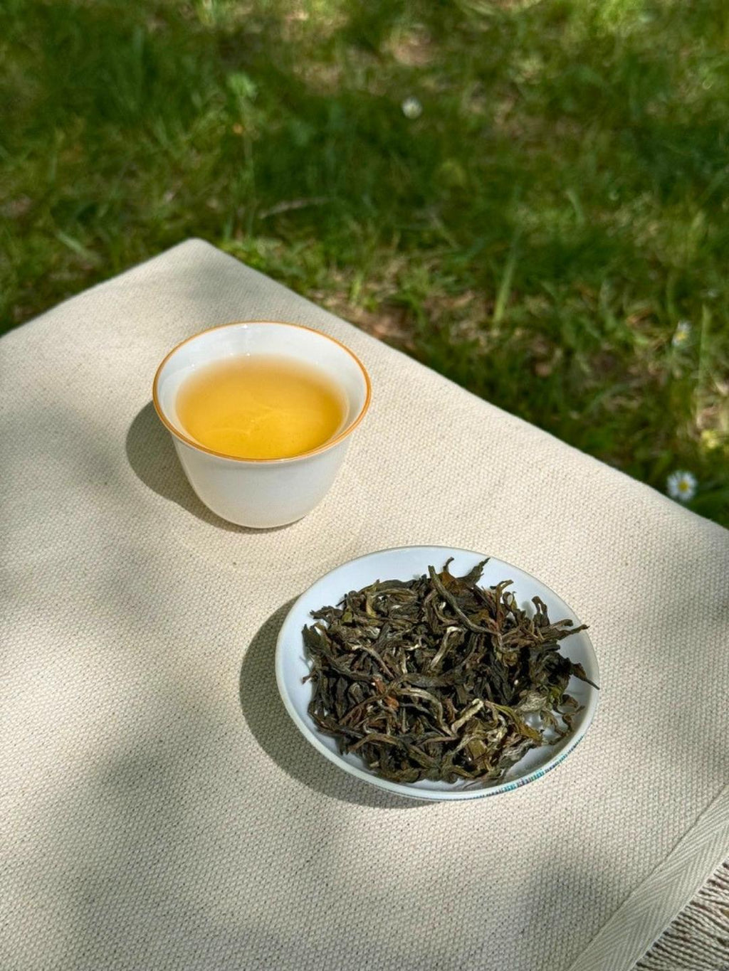 Spring Delight First Flush pale golden liquor in a ceramic cup beside whole leaf Himalayan tea on linen