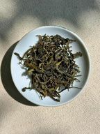 Whole dark green Spring Delight T78 & AV2 First Flush tea leaves with silvery fuzzy buds on a white ceramic plate