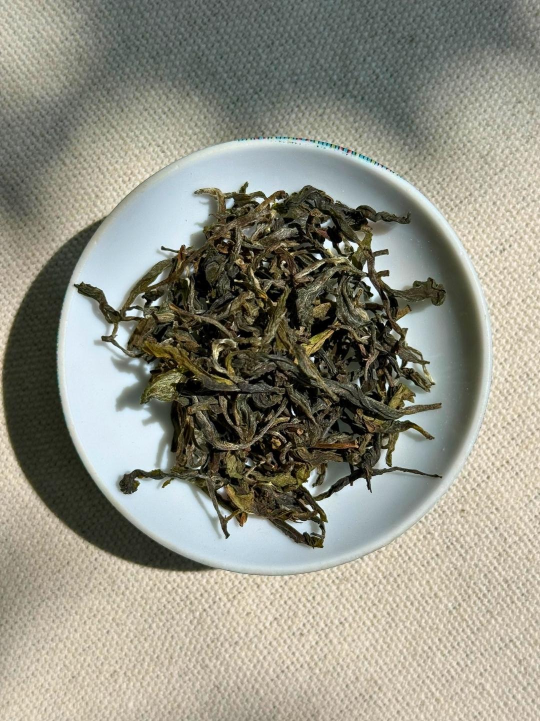 Whole dark green Spring Delight T78 & AV2 First Flush tea leaves with silvery fuzzy buds on a white ceramic plate
