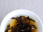 Velvet Muscatel, ein Oolong mit Insektenbiss, zieht in einem weißen Gaiwan, dunkle Blätter in einem honiggoldenen Aufguss
