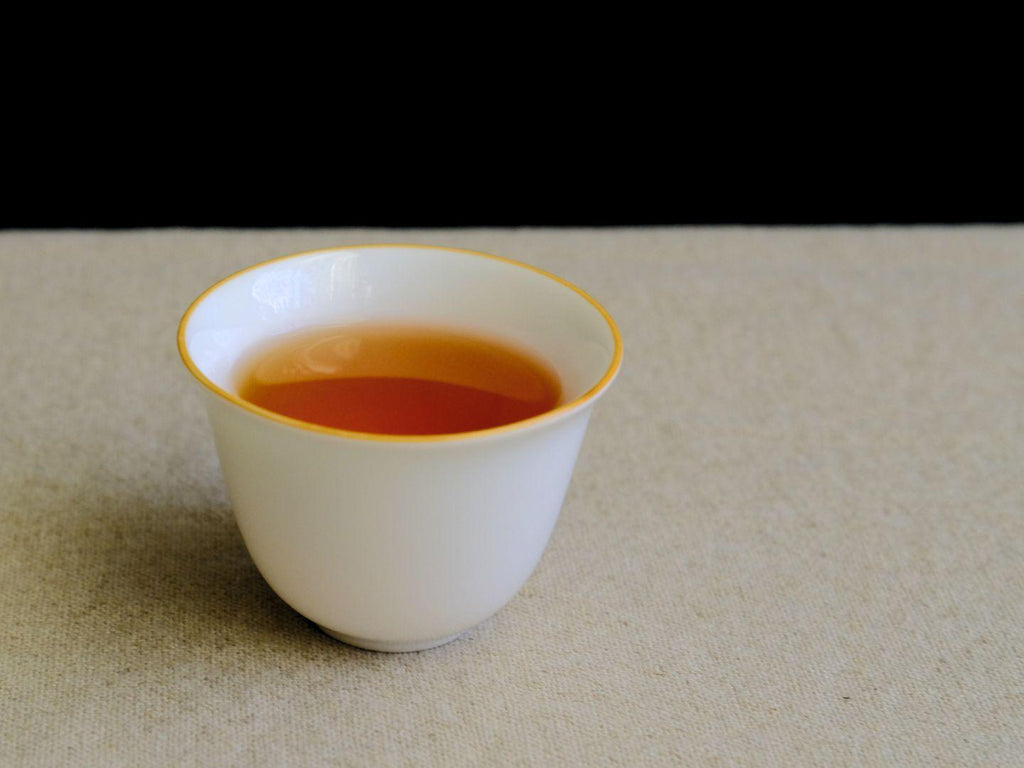 Eine Tasse Velvet Muscatel Oolong, bernsteinfarben mit Noten von karamellisierten Äpfeln, in einer weißen Tasse mit Goldrand
